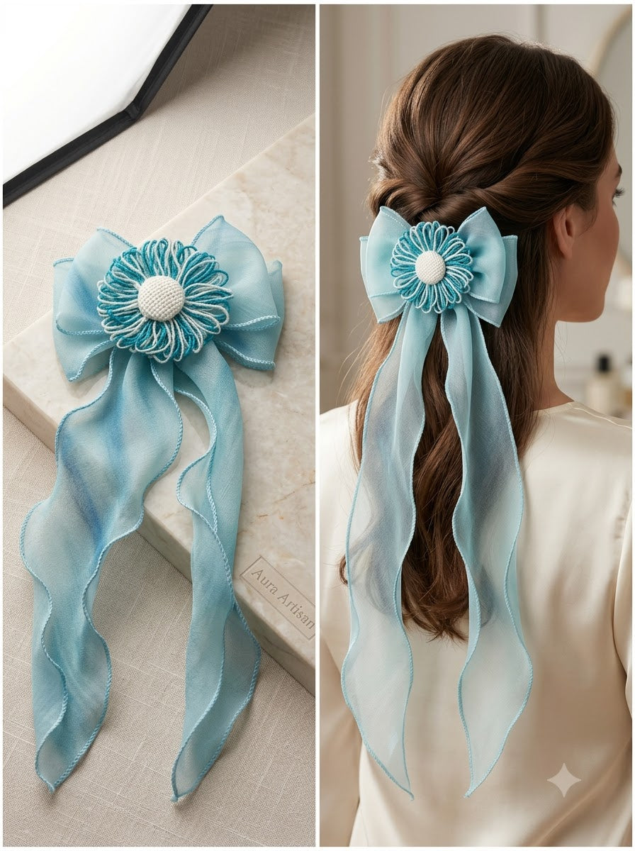 Aqua blue chiffon bow clip with teal thread daisy and pearl bead centre shown as product flat lay and styled on half-up ponytail