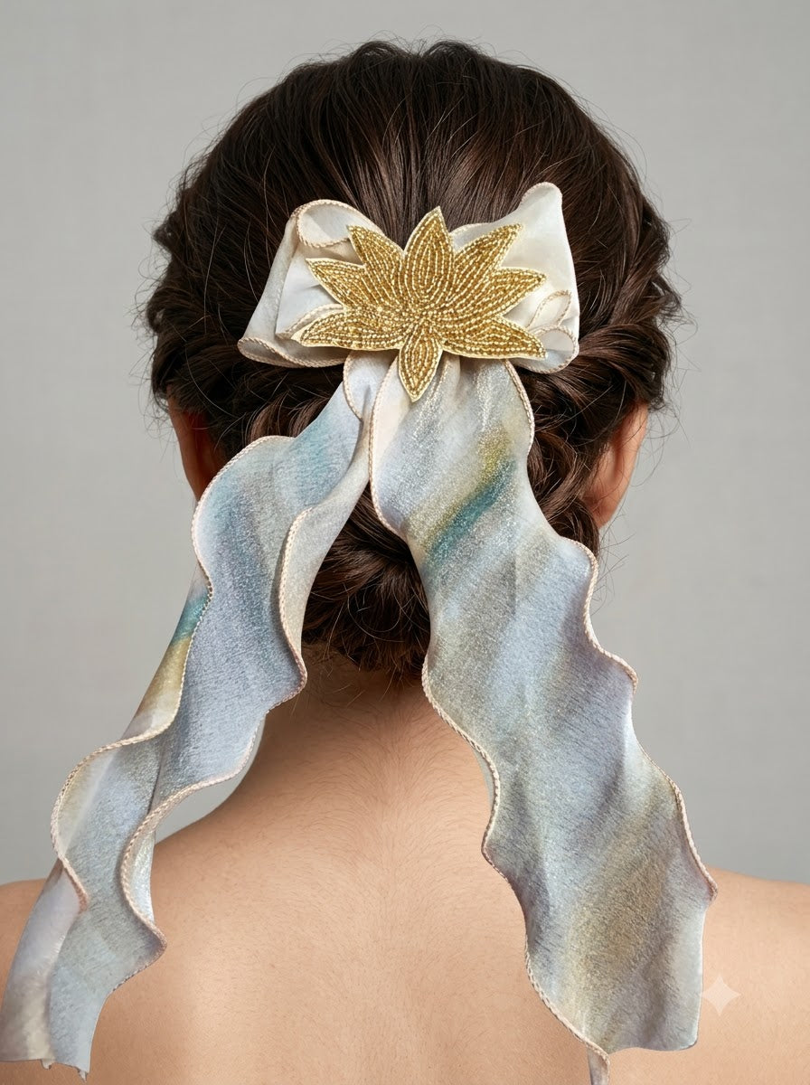 Ivory and iridescent blue organza bow barrette with gold zardozi lotus embroidery styled on low twisted bun on dark hair