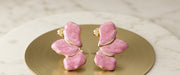 Pair of pink marbled enamel butterfly stud earrings with gold-tone edge displayed on a gold disc against a marble background