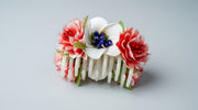 Floral hair claw clip with pink carnation blooms, white orchid with blue berry centre and green leaf accents on a cream claw base