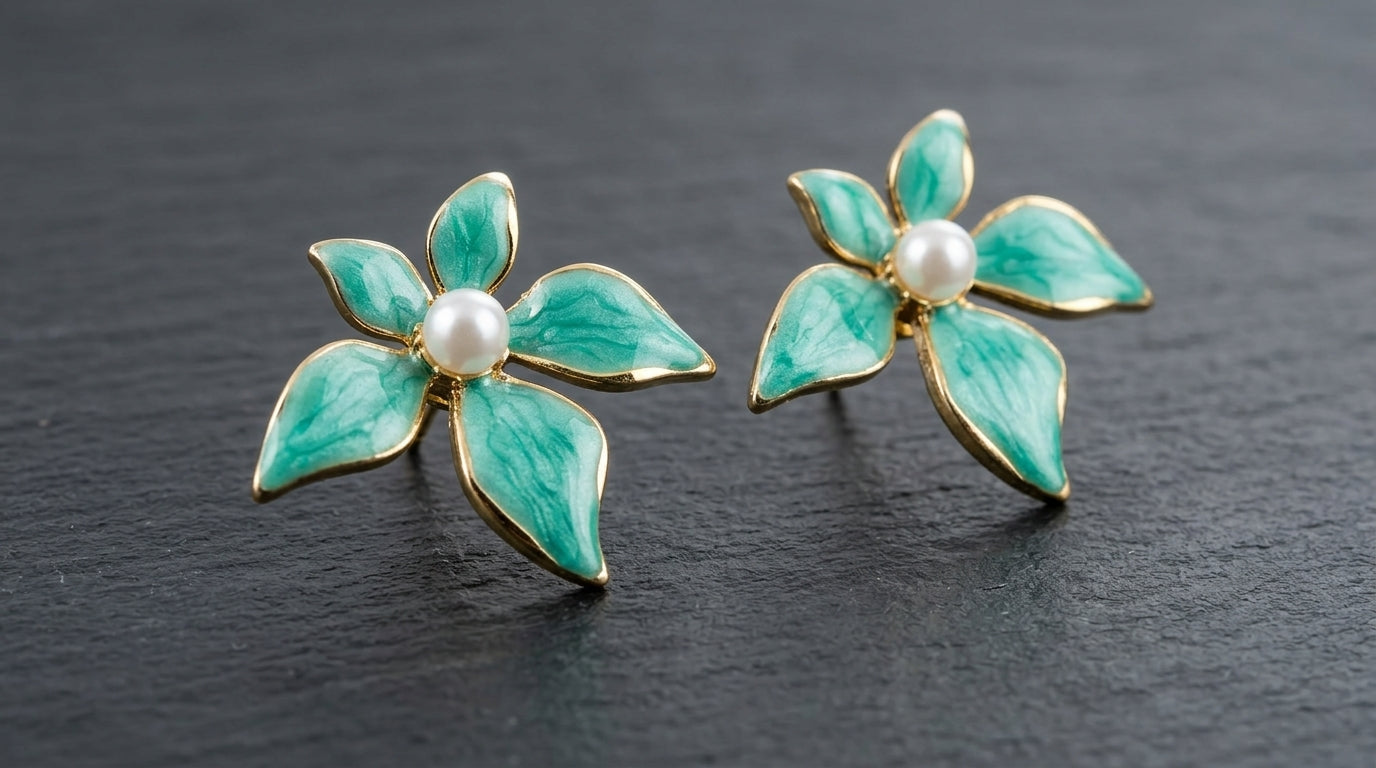 Pair of teal marbled enamel four-petal flower stud earrings with pearl centre and gold-tone outline on a dark slate background